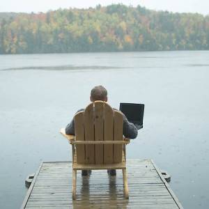 Remote working man with laptop beside lake