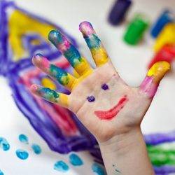 A child's hand shows creativity covered in many paint colours and a smiling face