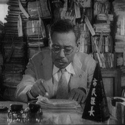 A still from the movie Ikiru in which the protagonist is sitting at a desk