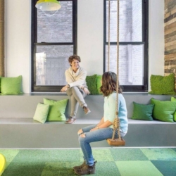 Two women talking in a pleasant and well designed office, one on a bench the other a swing, to illustrate the importance of wellbeing