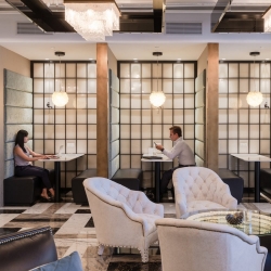 Two people working separately in neighbouring booths in an office to illustrate the principle of third place facilities in hybrid working cultures. 