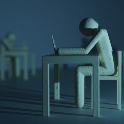 A wood carving of a blank, slumped person sitting at a desk with a laptop to depict the dehumanization potential of smart technology