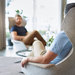 A middle aged man and a younger male colleague sit in comfortable chairs having a conversation to illustrate a conversation between generations of workers